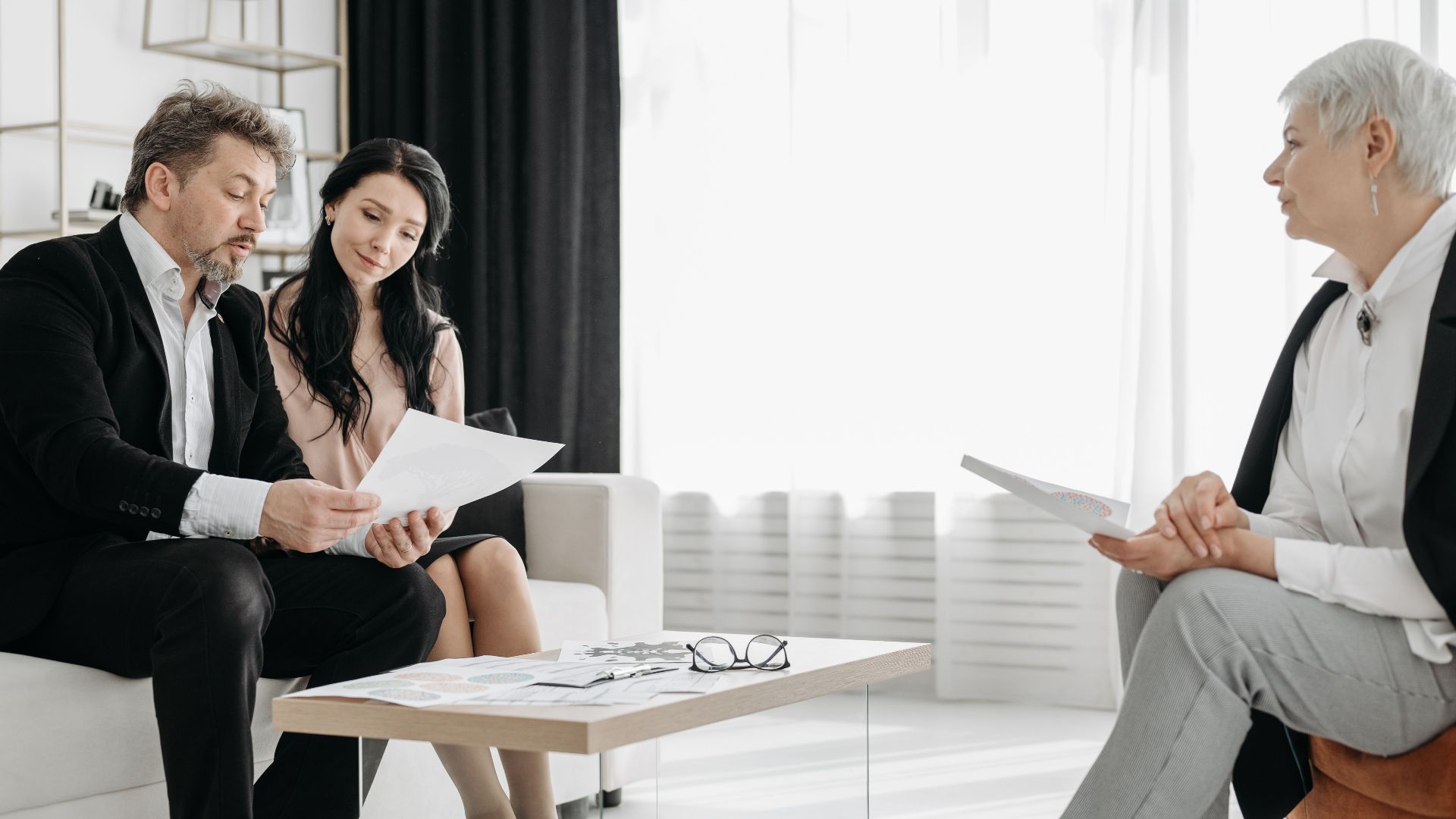 Business meeting in a modern lounge with three adults discussing documents.