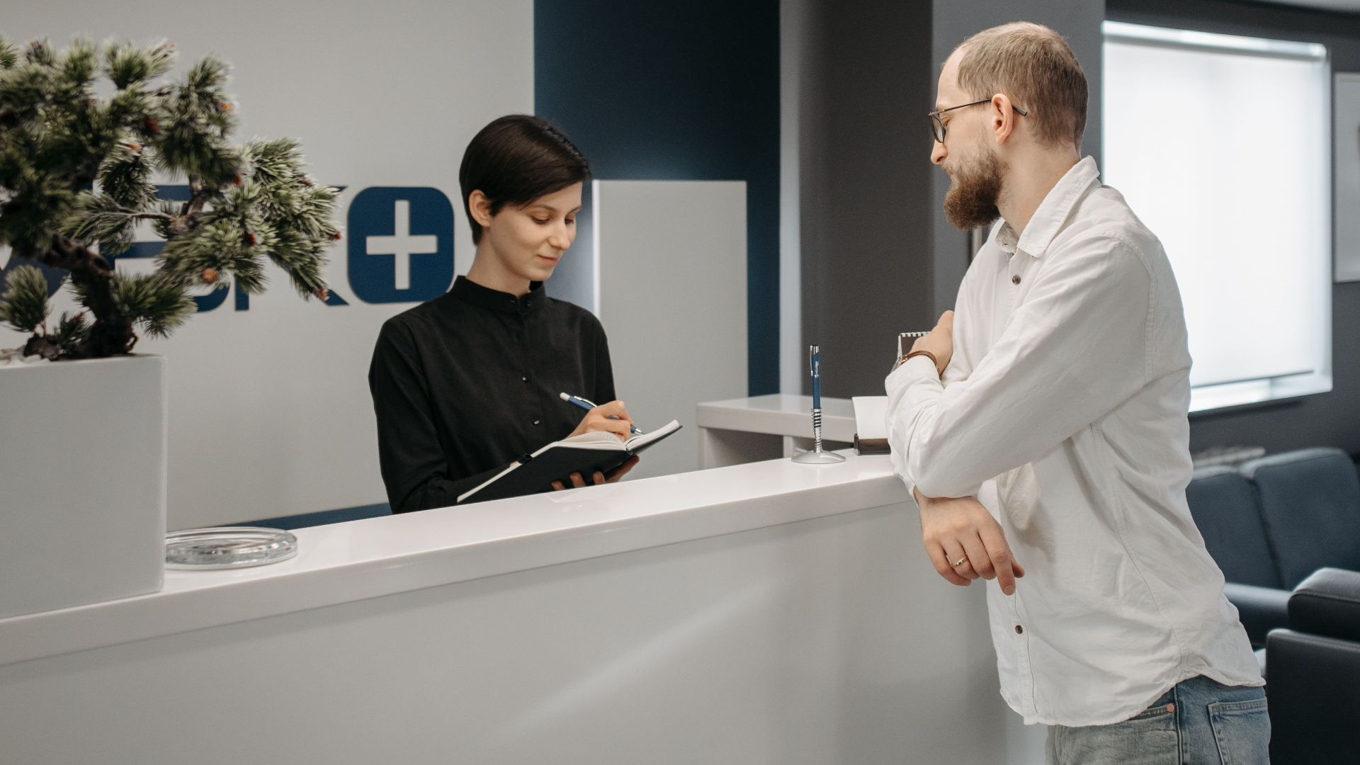 A man consults a receptionist in a modern clinic setting with contemporary design.