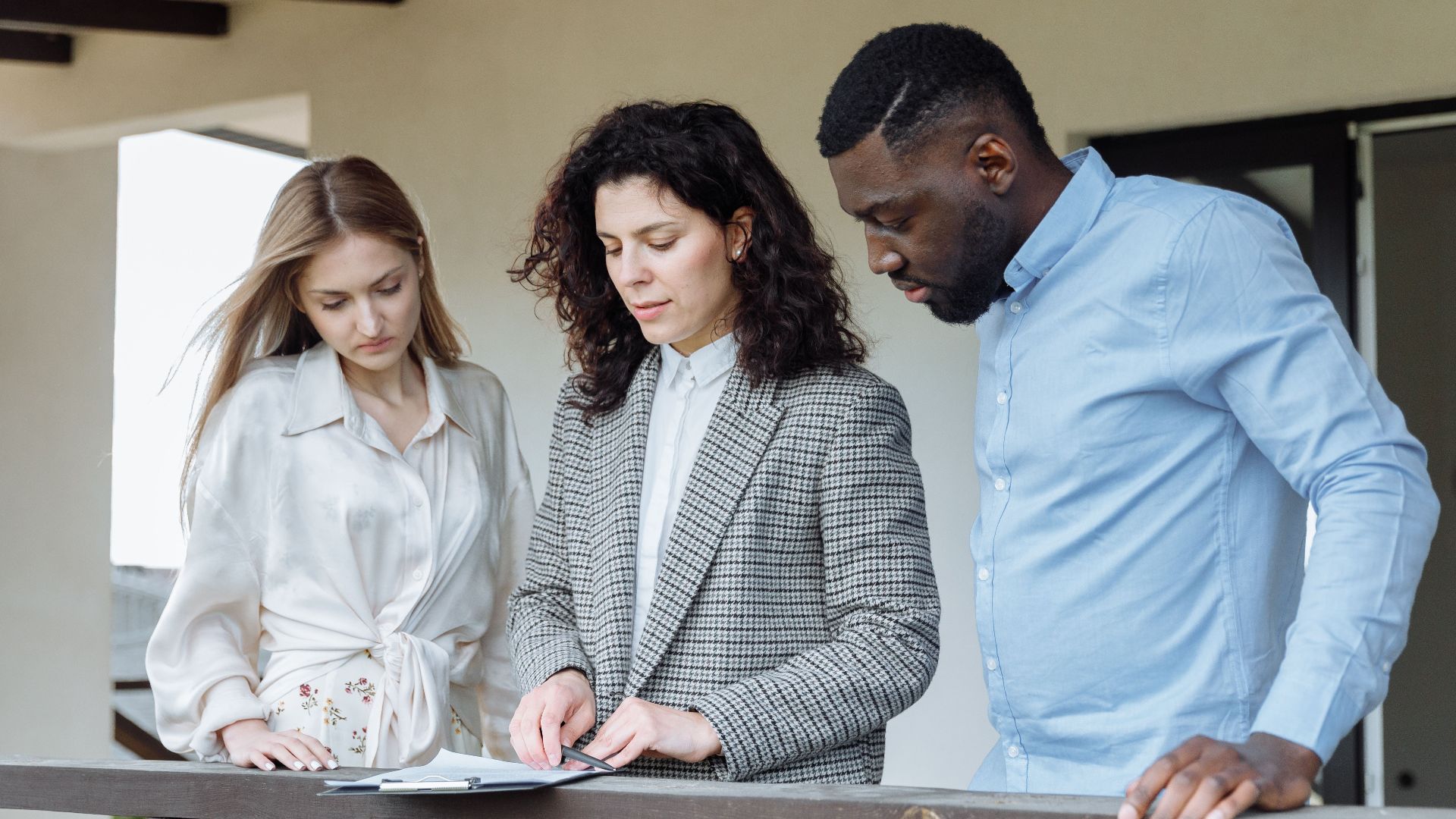 Three adults reviewing documents on a balcony during a real estate consultation.