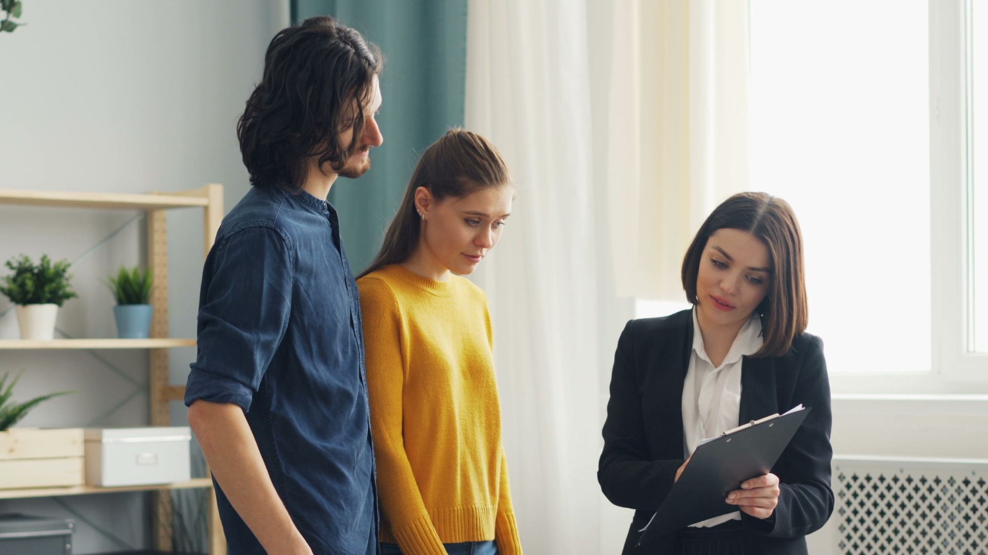Real estate agent consulting a couple in a modern living room setting, surrounded by indoor plants.