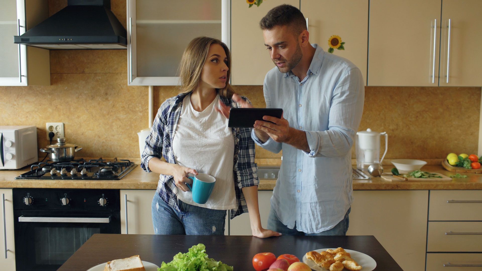 A couple discusses meal plans in a modern kitchen using a tablet.