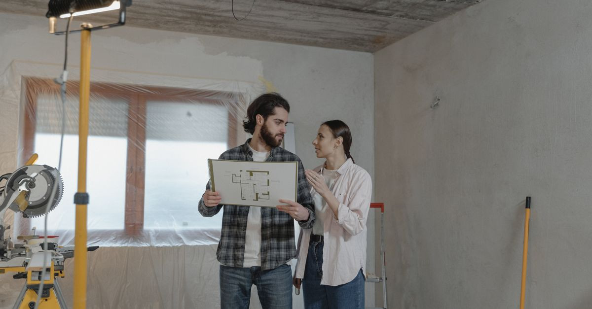 A couple reviews a blueprint in a partially renovated room, planning home improvements.