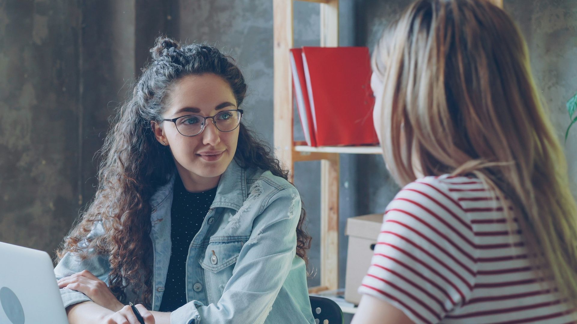 Two women are having a conversation at a desk