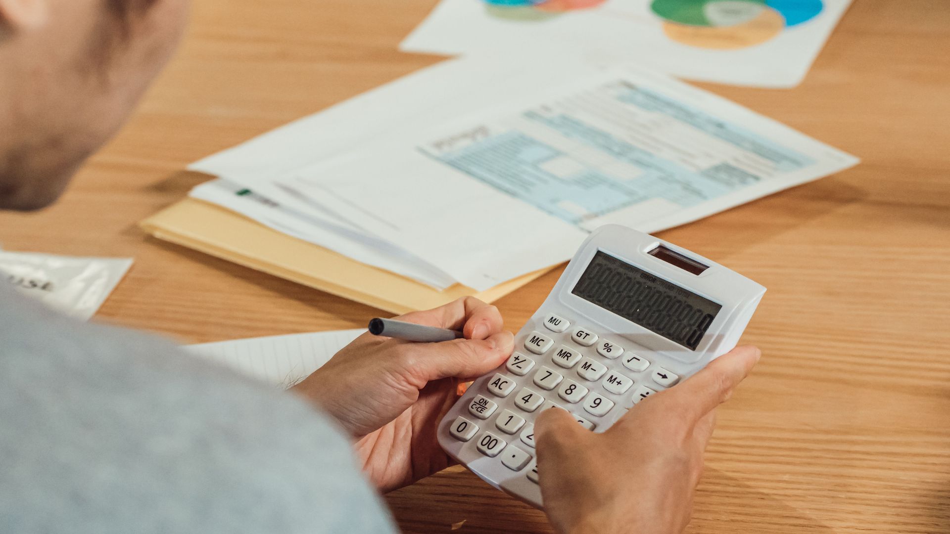 Person using a calculator at a desk with financial documents. Modern business concept.