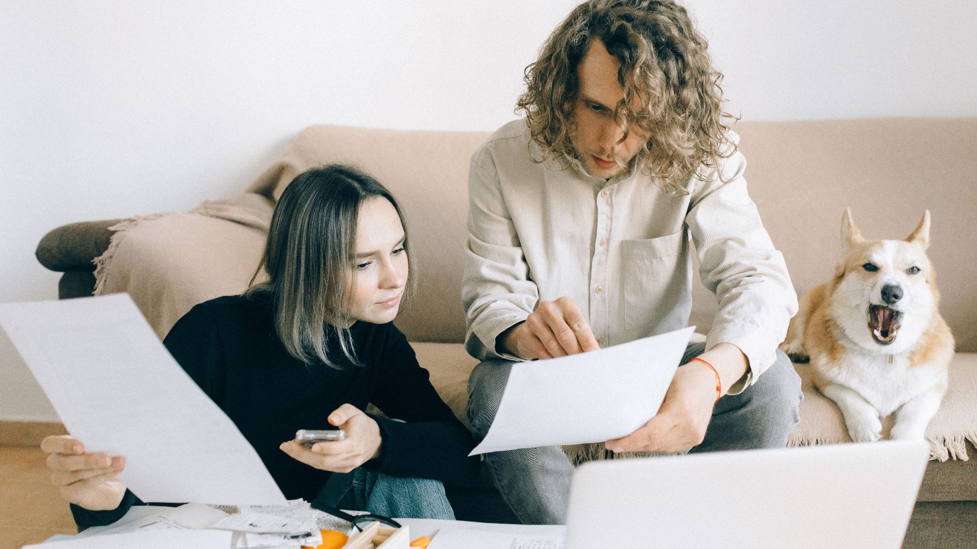 A couple working remotely at home with documents and a dog on the sofa.