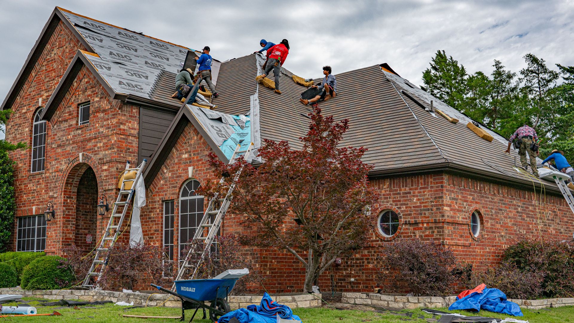 Roofers working on brick home in Allen, Texas, addressing shingles and roofing materials.
