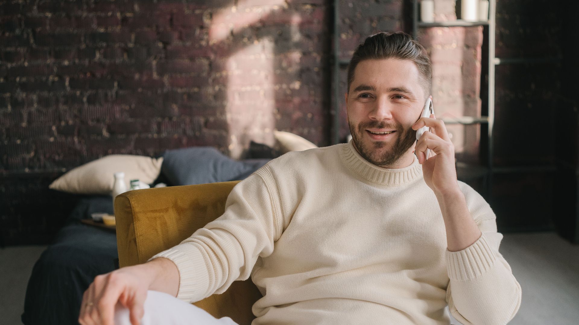 Smiling man in a cozy setting, enjoying a phone call while seated indoors.
