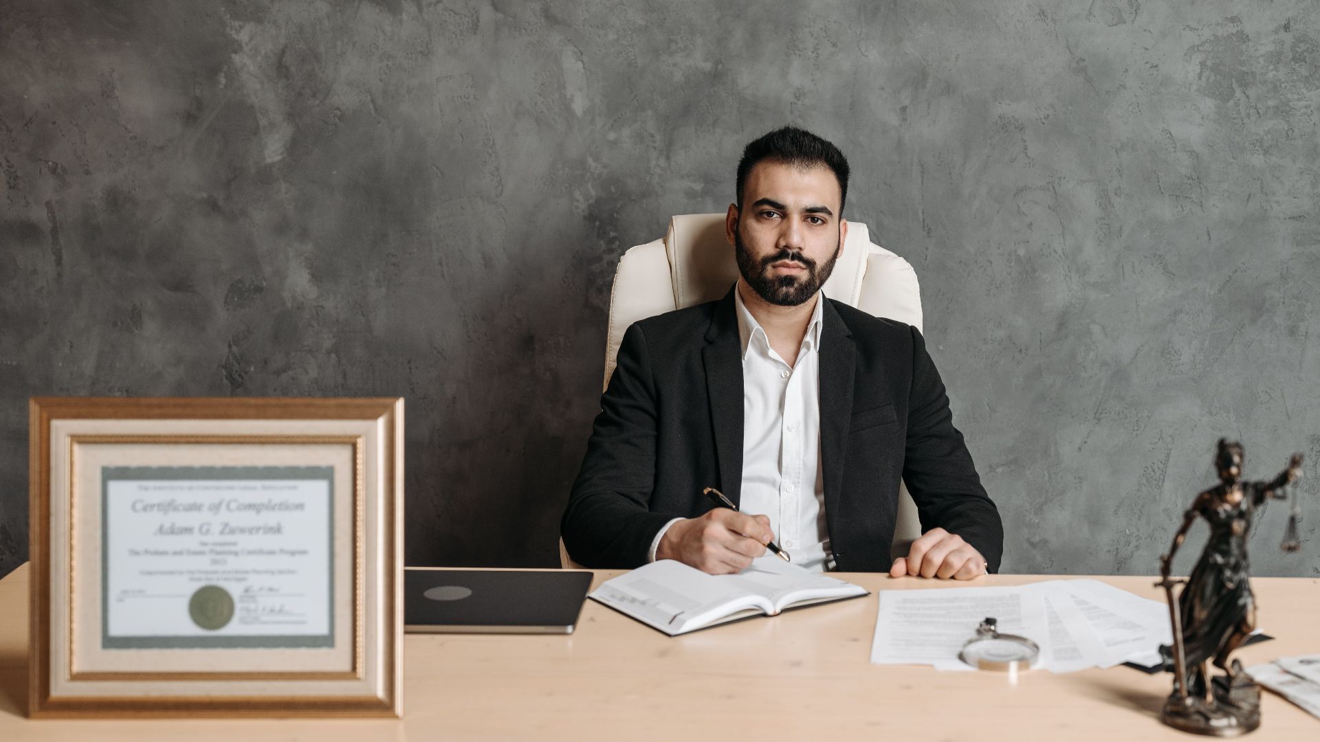 Confident man sitting at a desk surrounded by legal documents and a certificate.