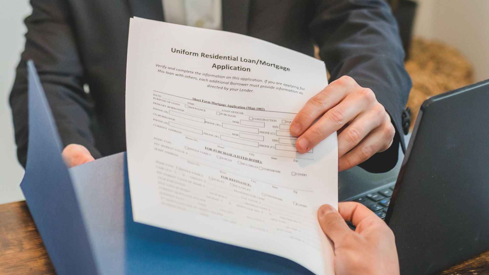 Professional setting showing hands exchanging a mortgage application document indoors.