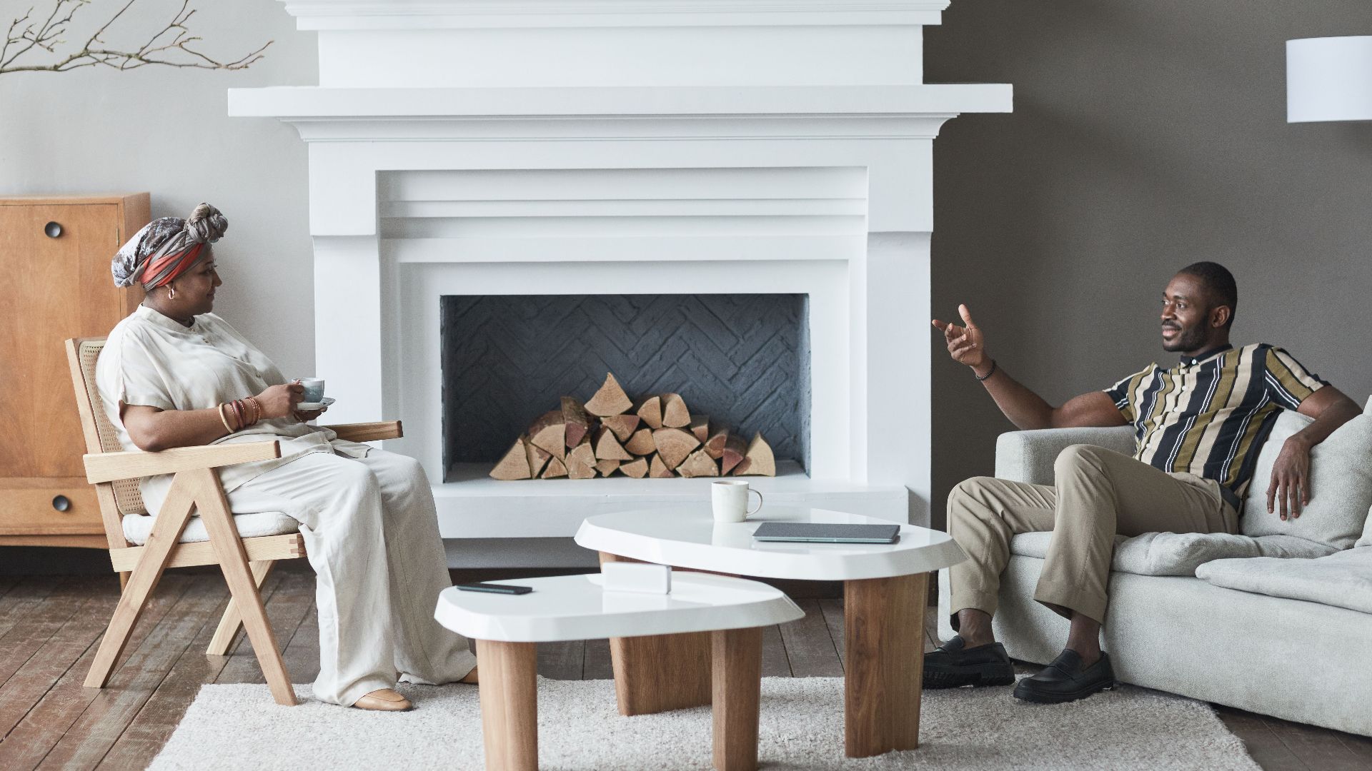 Two adults having a relaxed conversation in a stylish living room with a modern fireplace.