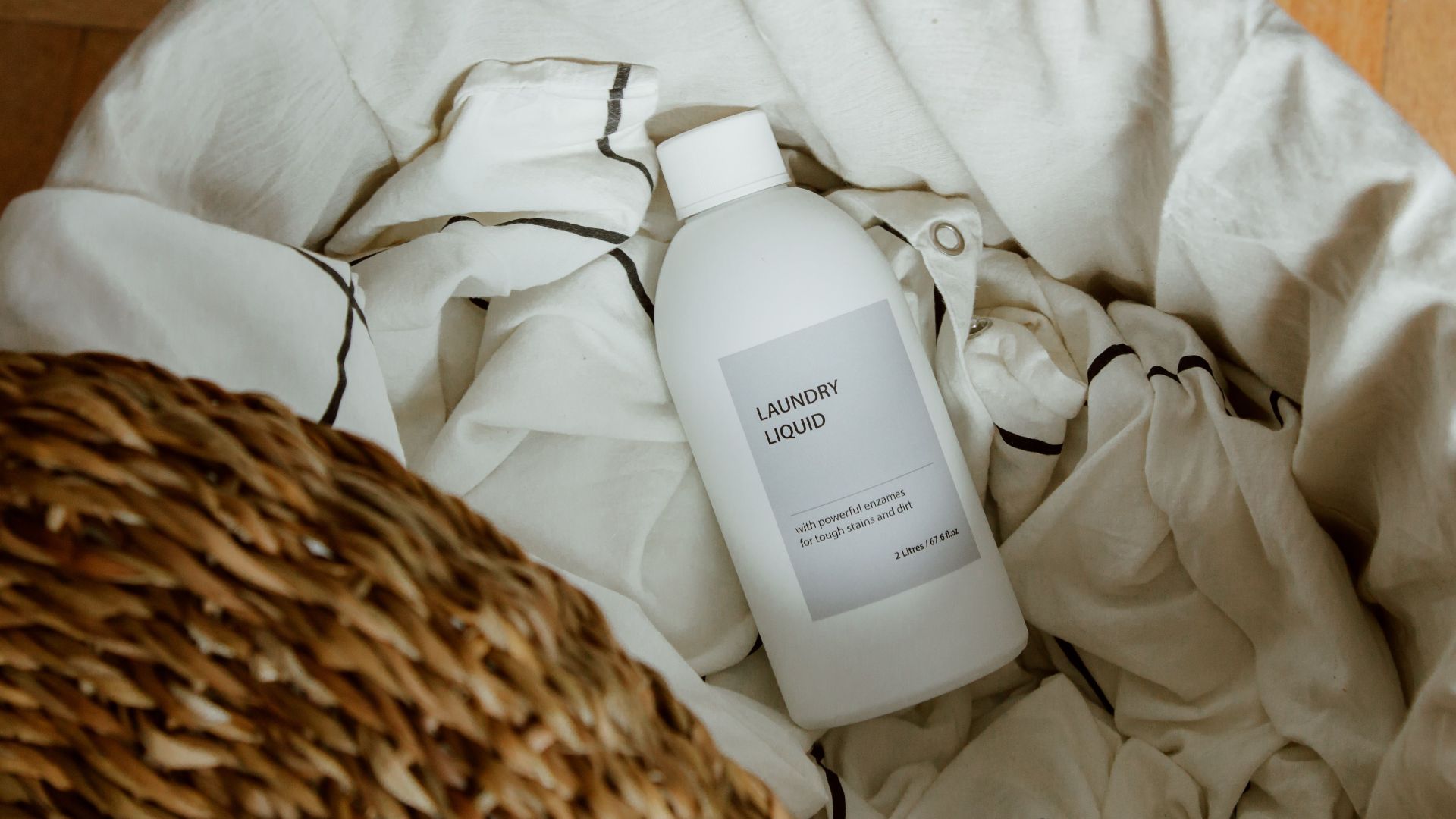 High angle view of laundry liquid in basket with white linens on wooden floor.