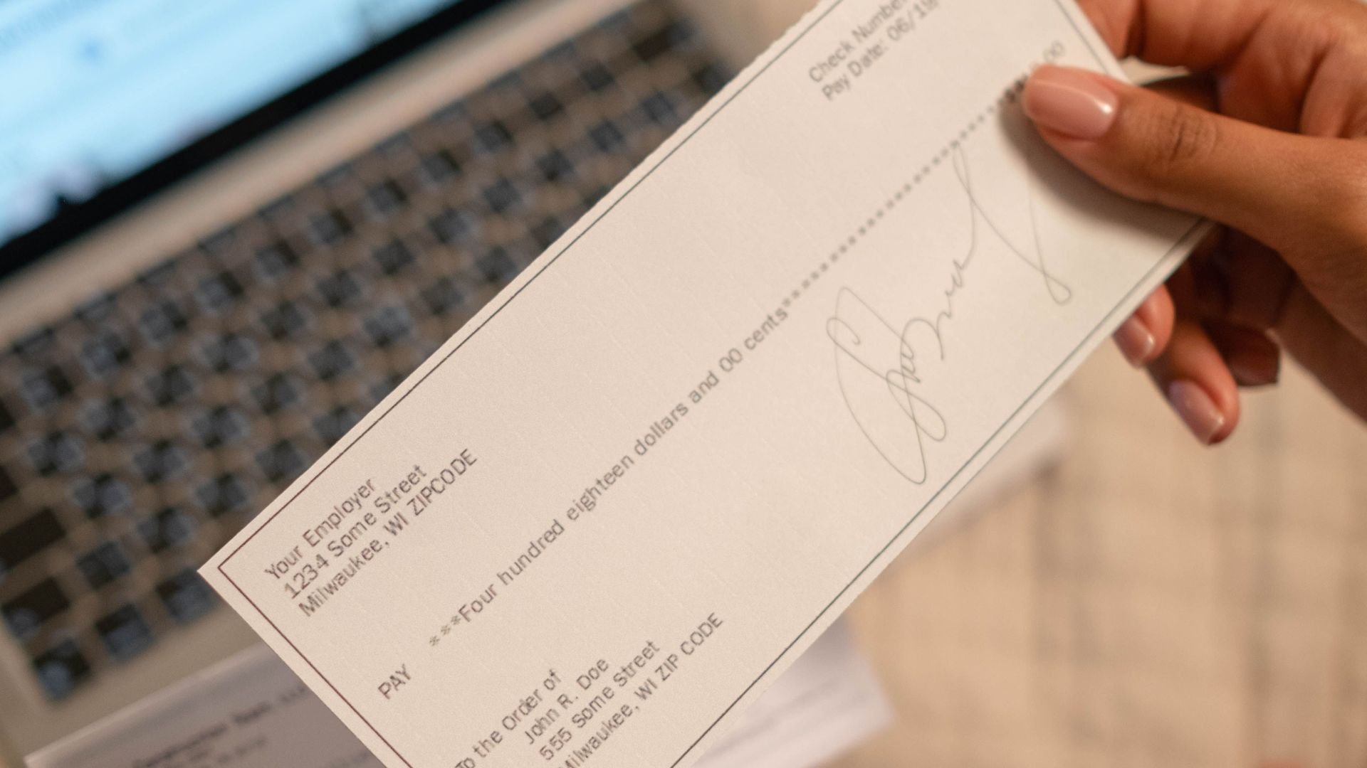 Individual holding a cheque over laptop, signifying online banking or financial transaction.