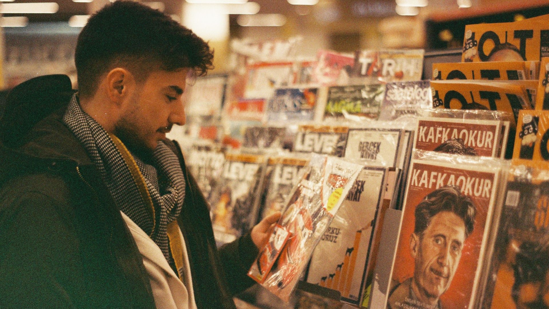 A young man browsing and selecting magazines from a rack in a store.