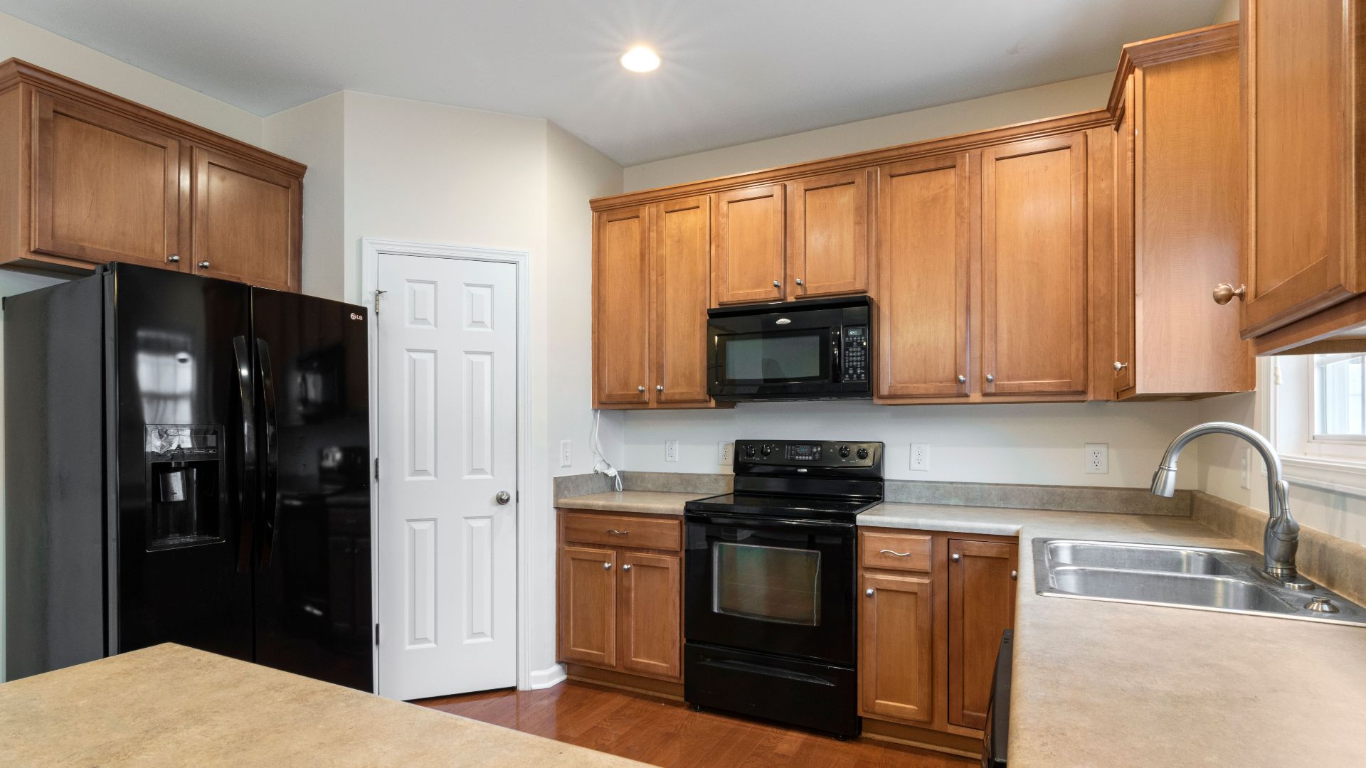 A spacious kitchen featuring wooden cabinets, black appliances, and a sleek countertop.