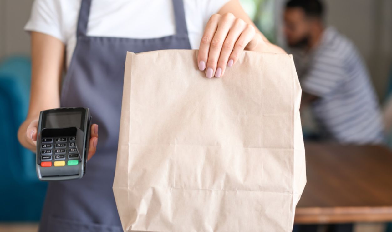 Young waitress with food for delivery and payment terminal in restaurant