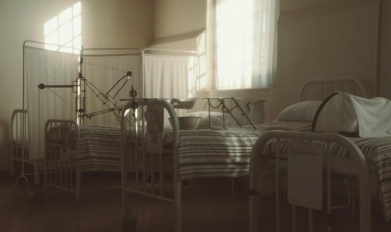 Dimly lit vintage hospital room featuring empty beds and medical equipment, creating a nostalgic atmosphere