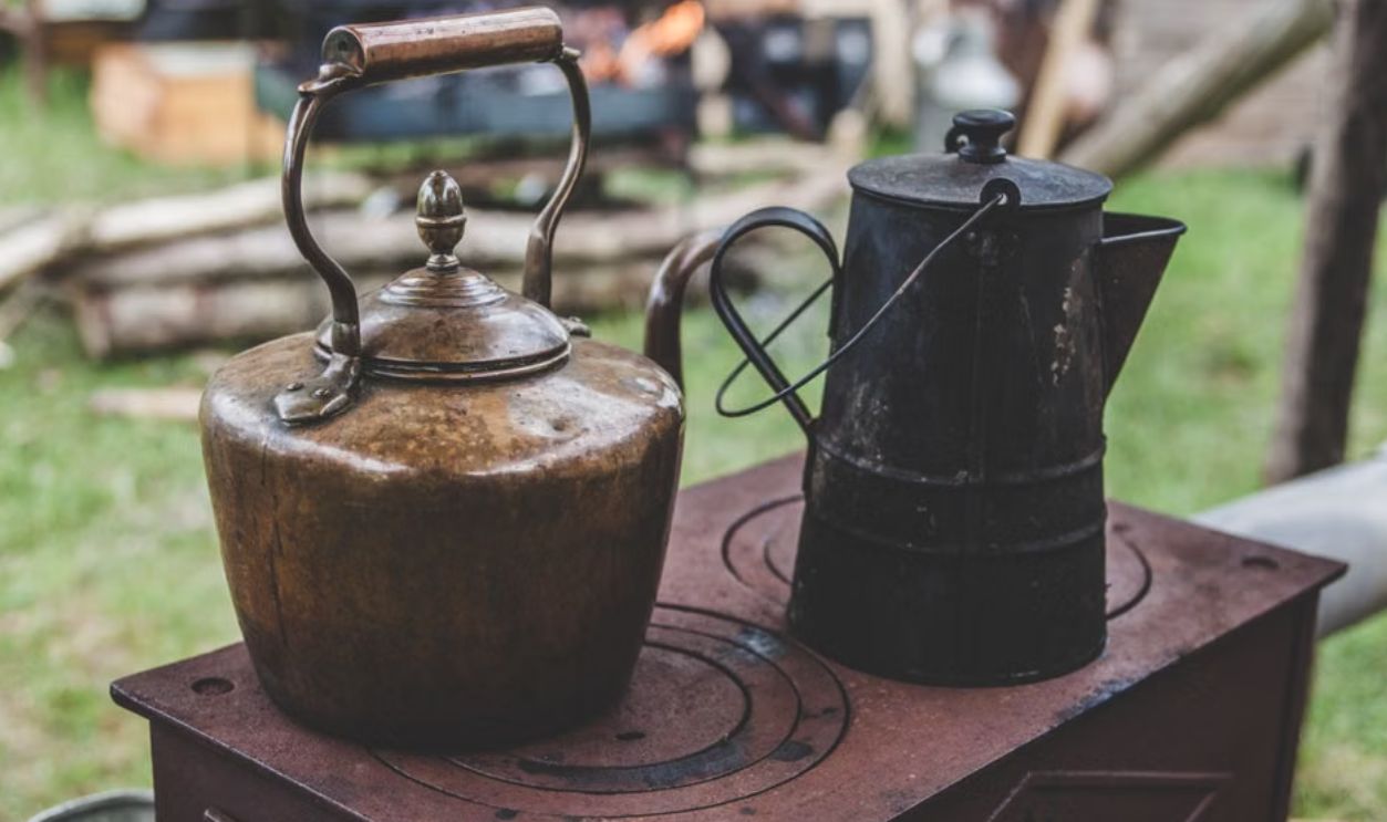 Vintage metal kettles on a rustic outdoor wood stove, creating a nostalgic rural scene