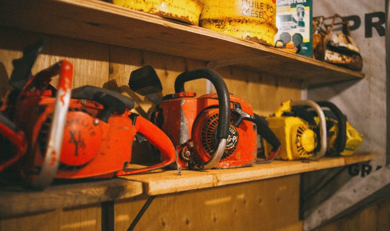 Collection of vintage chainsaws on a wooden shelf in a workshop setting.