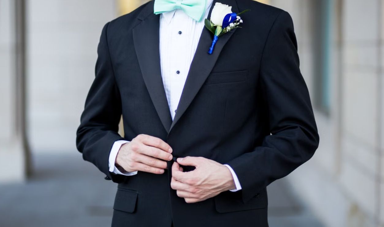 Sophisticated groom in a black tuxedo buttoning his jacket, adorned with a fresh boutonniere