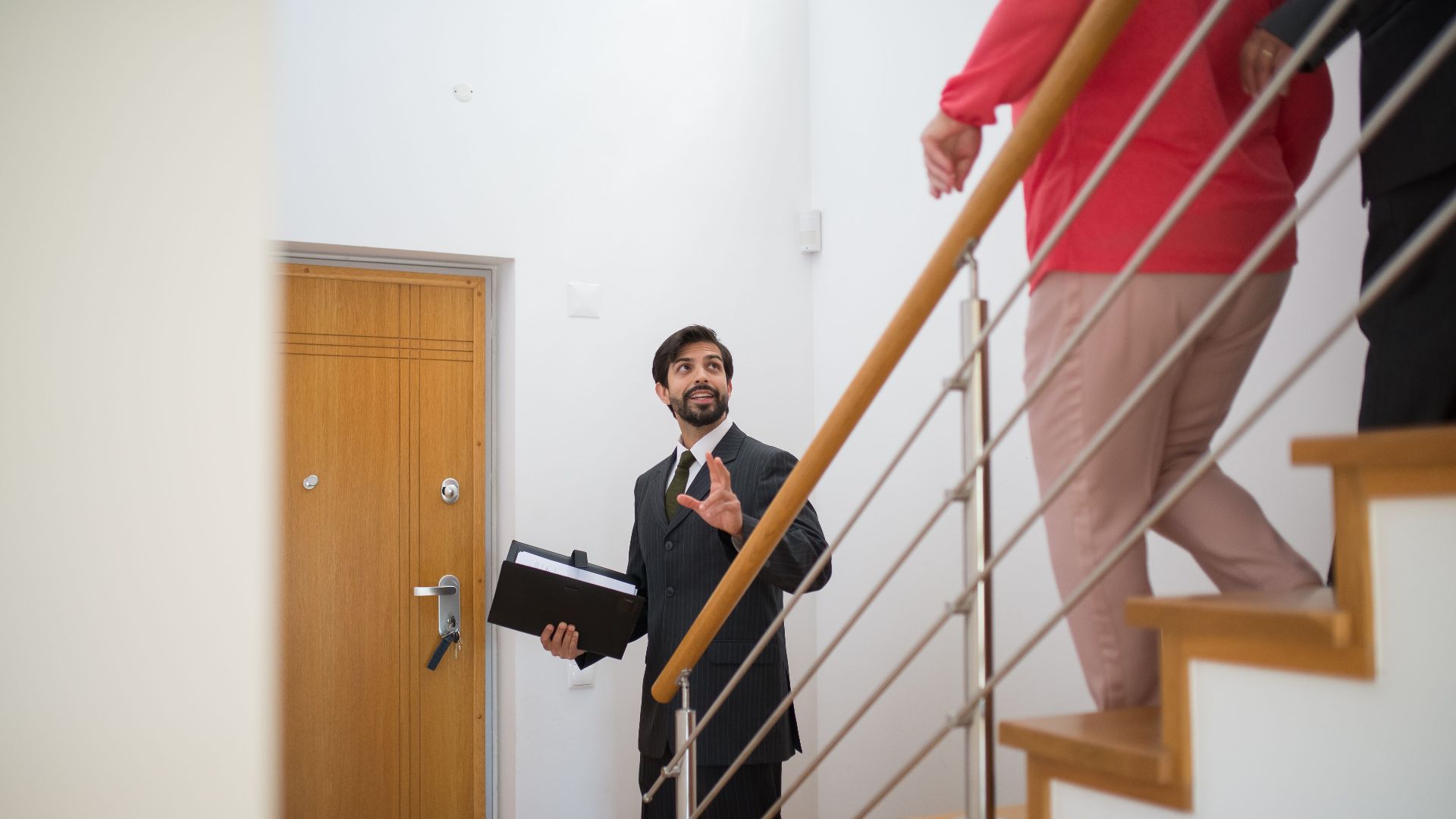 A realtor conducting a house tour with potential buyers on the stairs of a modern home.