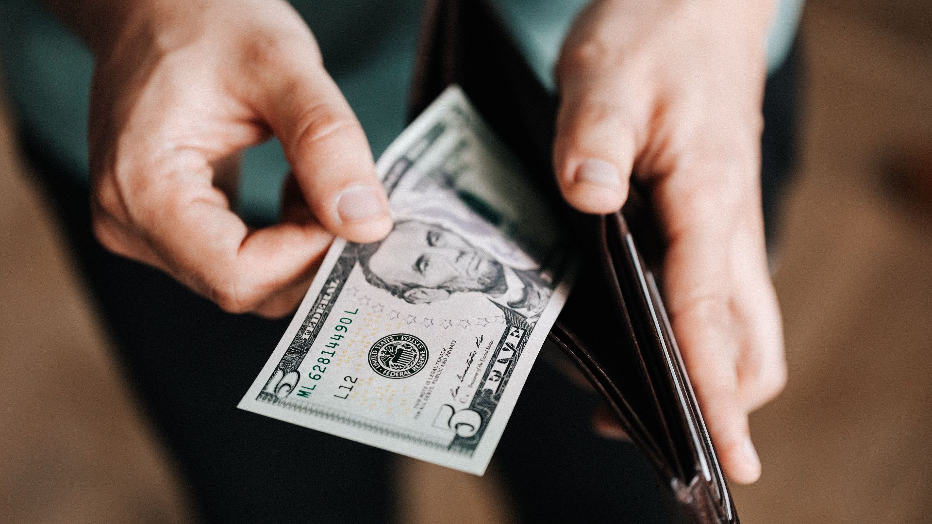 Closeup of crop male in casual clothes taking dollars out of wallet while paying in shop