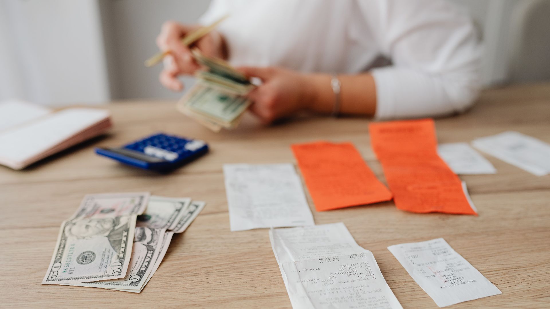 A person using a calculator and cash to plan a household budget.