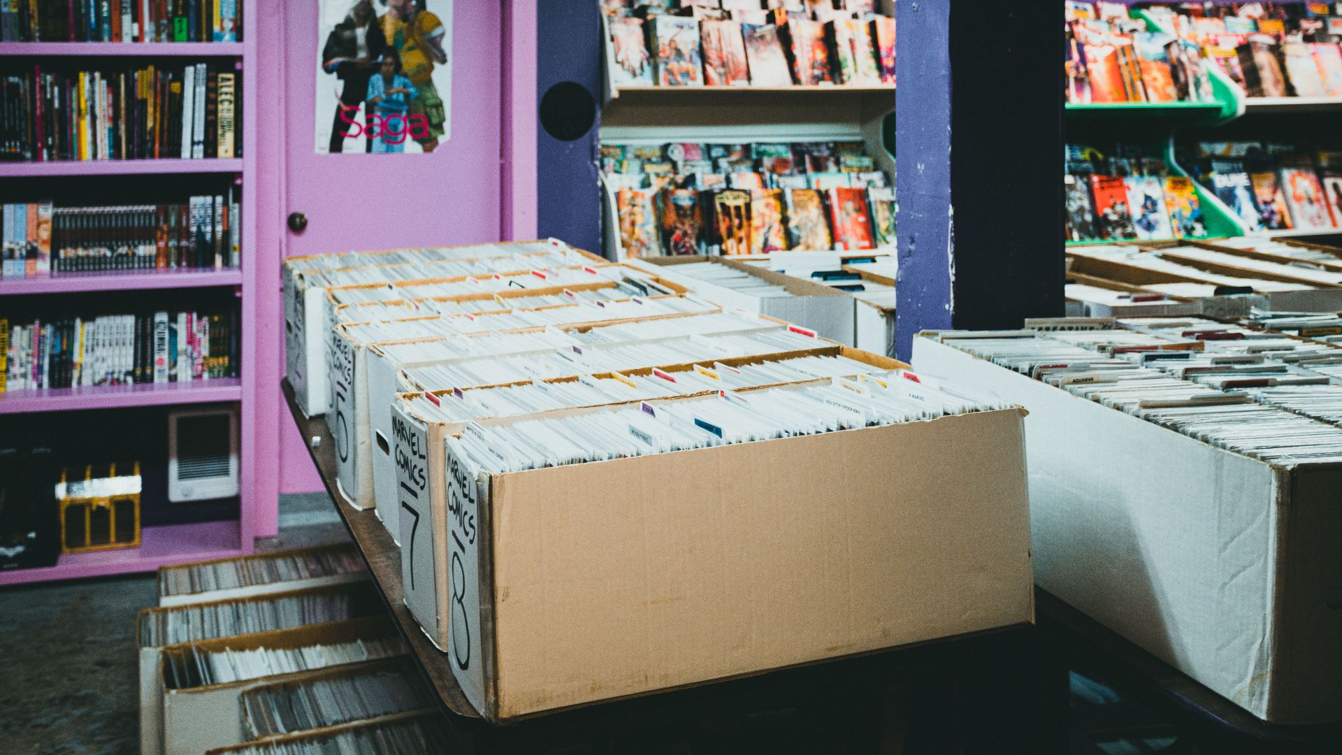 A colorful comic book store with organized shelves and boxes of comics for sale.
