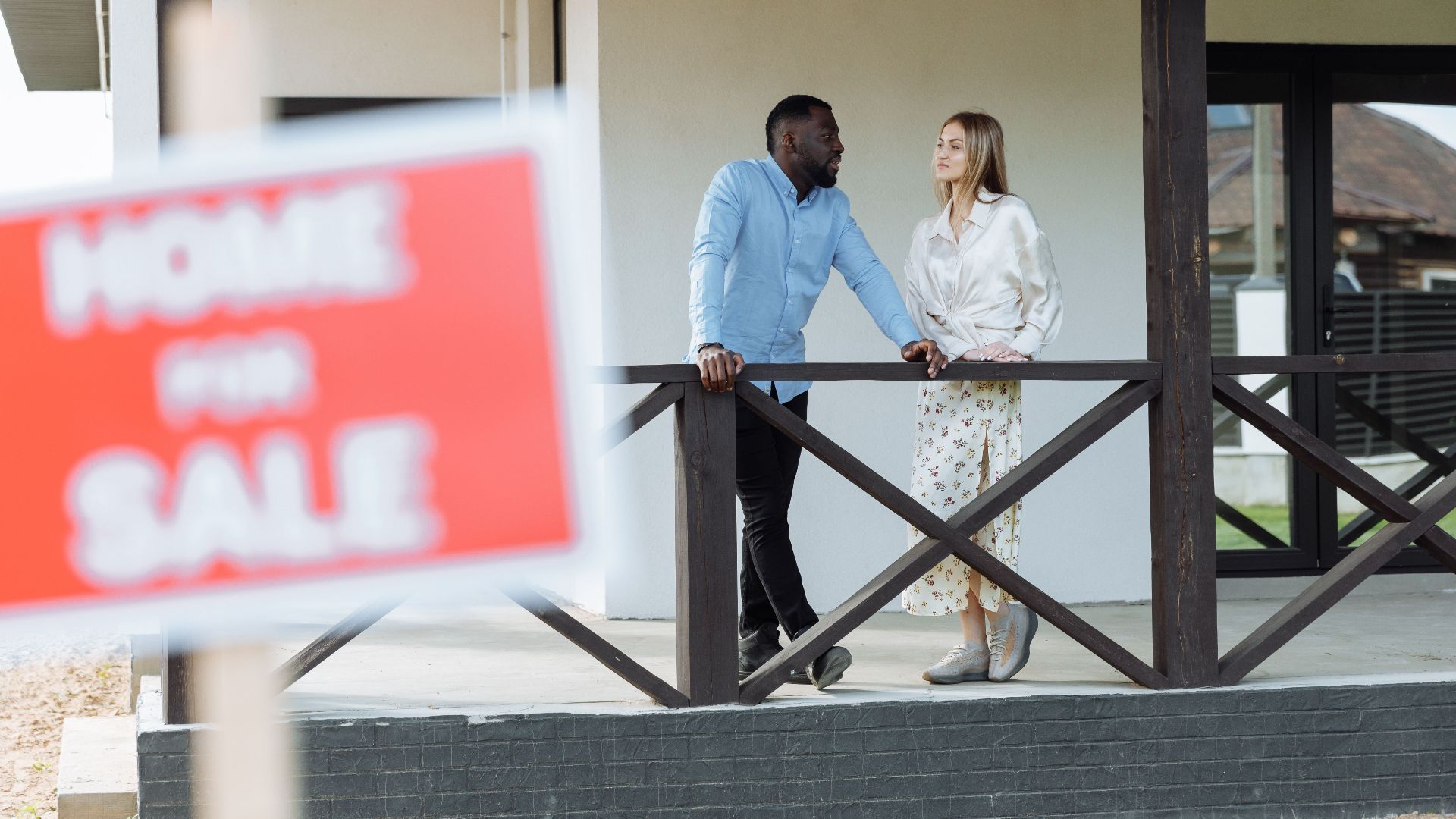 A black man and caucasian woman discussing a property for sale on a porch. Ideal for real estate content.