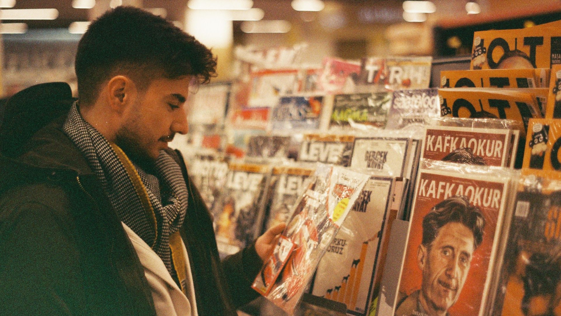 A young man browsing and selecting magazines from a rack in a store.