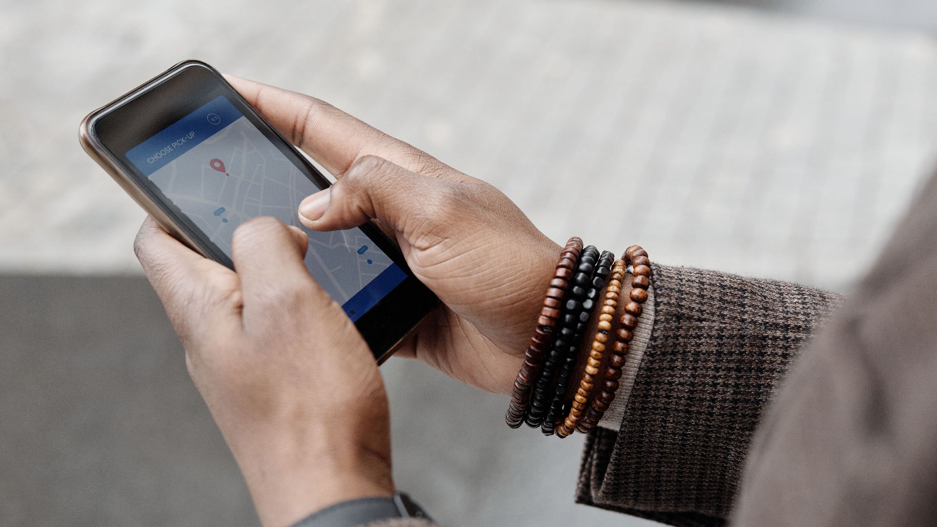 Close-up of hands with bracelets navigating on smartphone using GPS app outdoors.