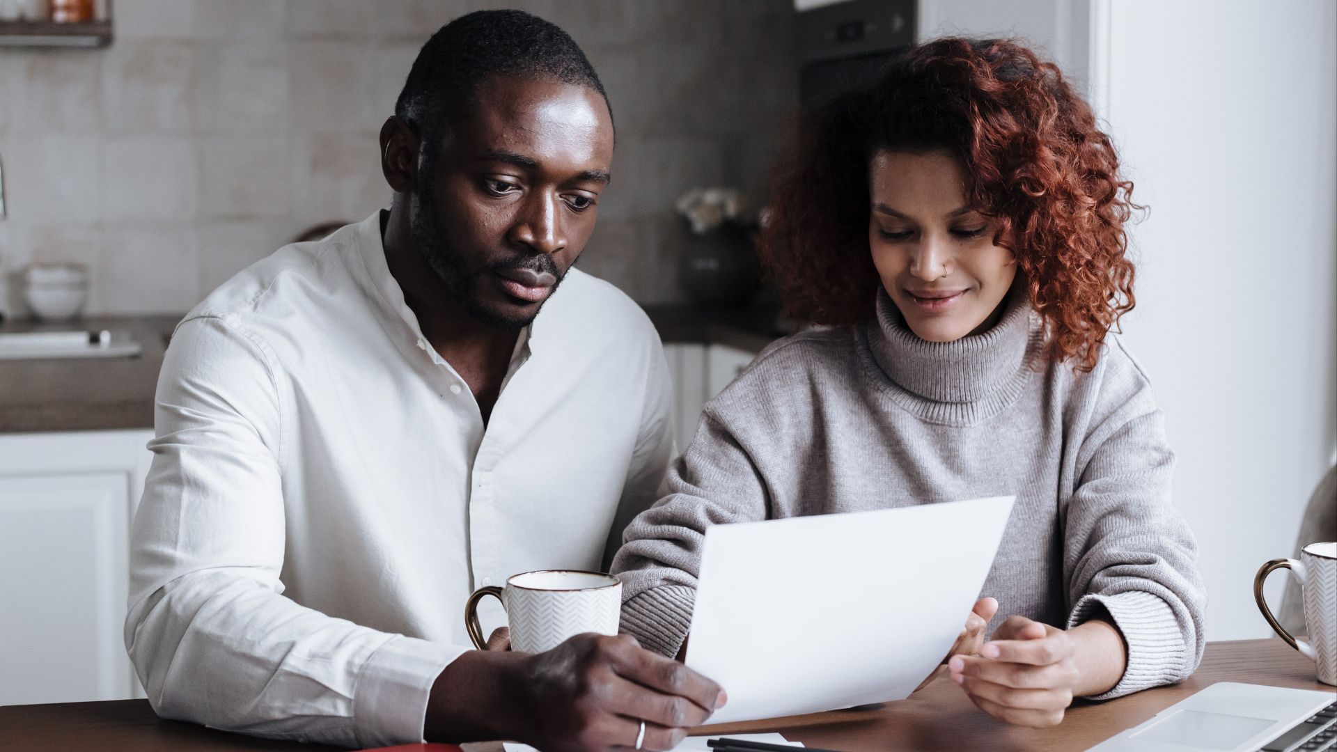 A couple reviews paperwork at a kitchen table, embodying teamwork and collaboration.