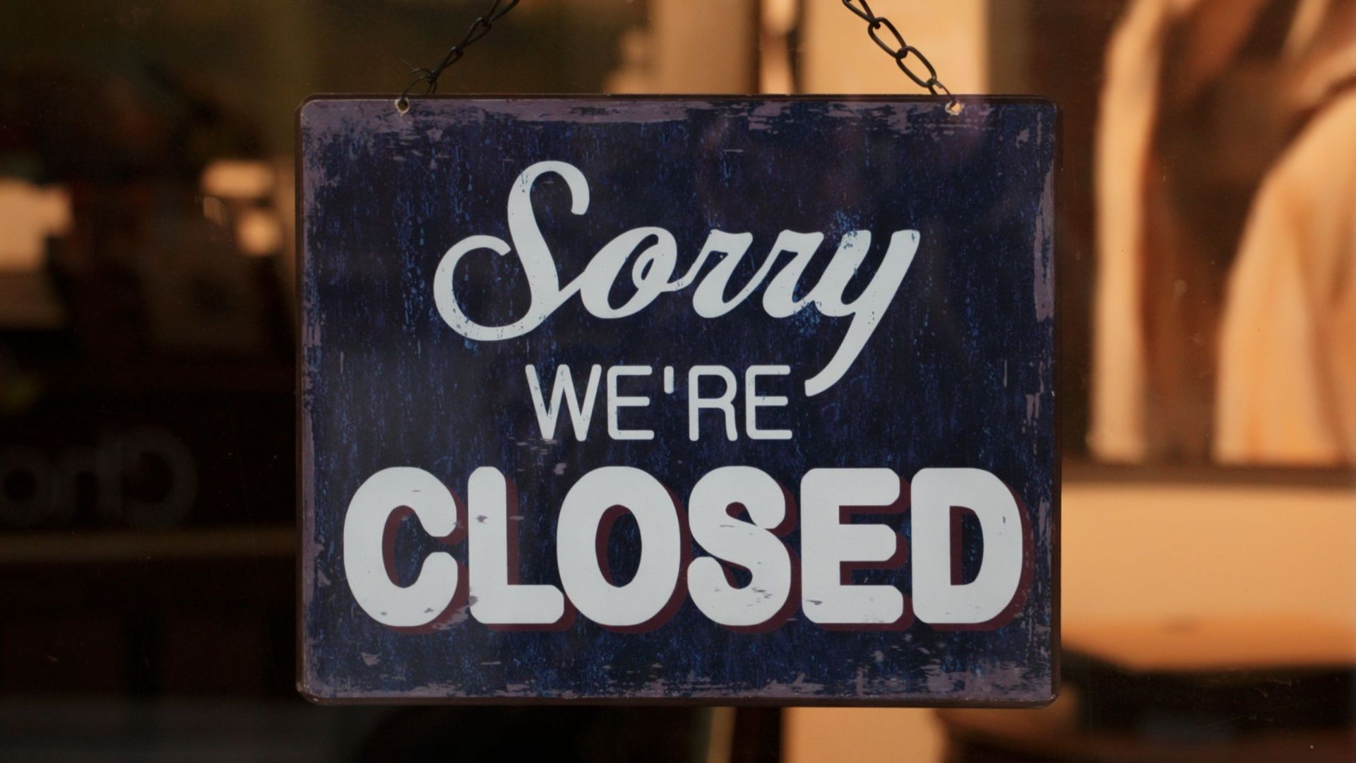 A 'Sorry We're Closed' sign hangs in a shop window, indicating closure.