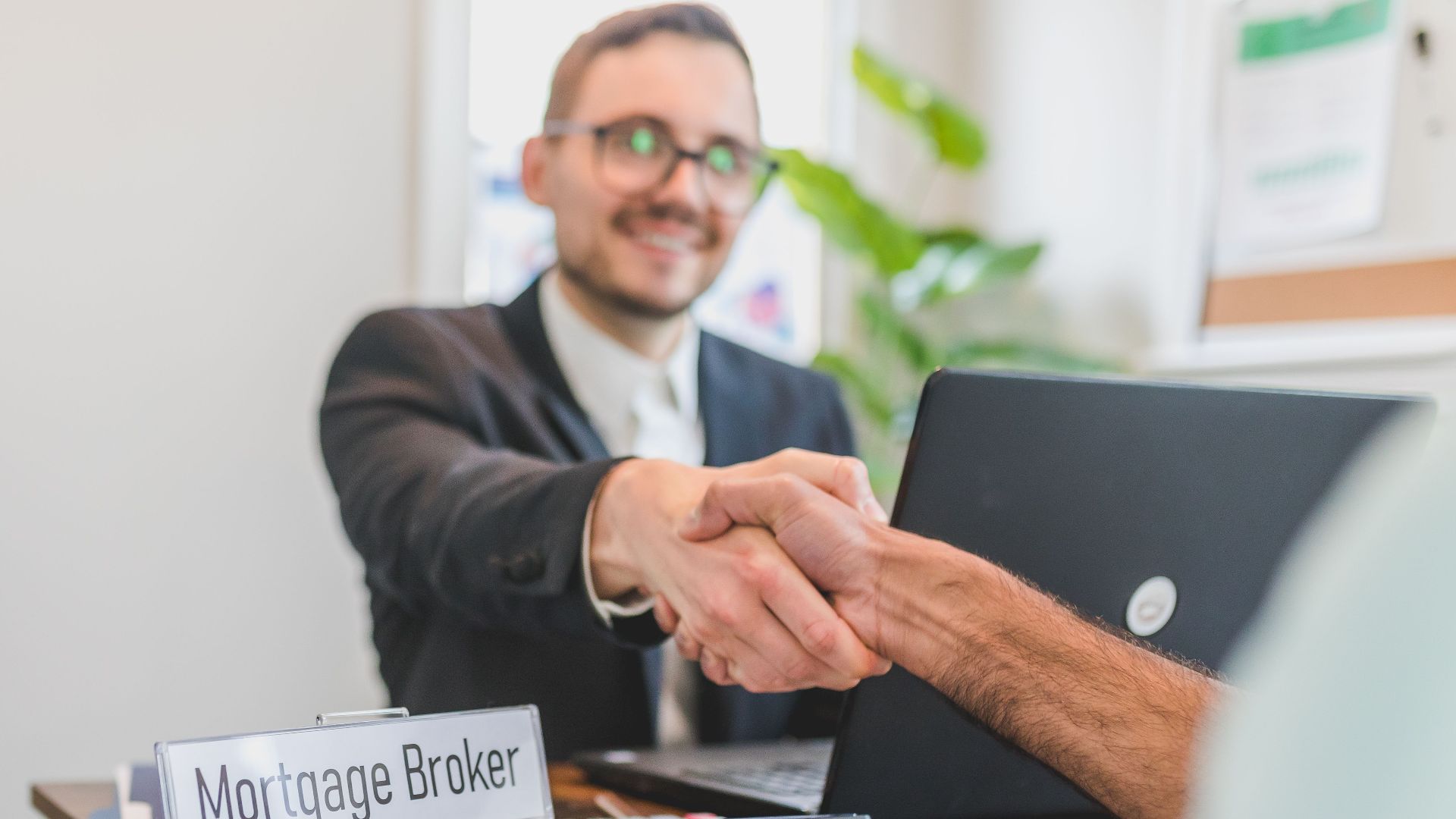 Mortgage broker and client sealing a deal with a handshake in a bright, modern office.