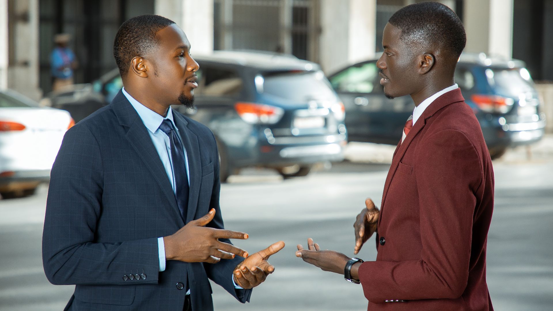 Two African businessmen in formal suits have a discussion on a city street in Dakar, Senegal.