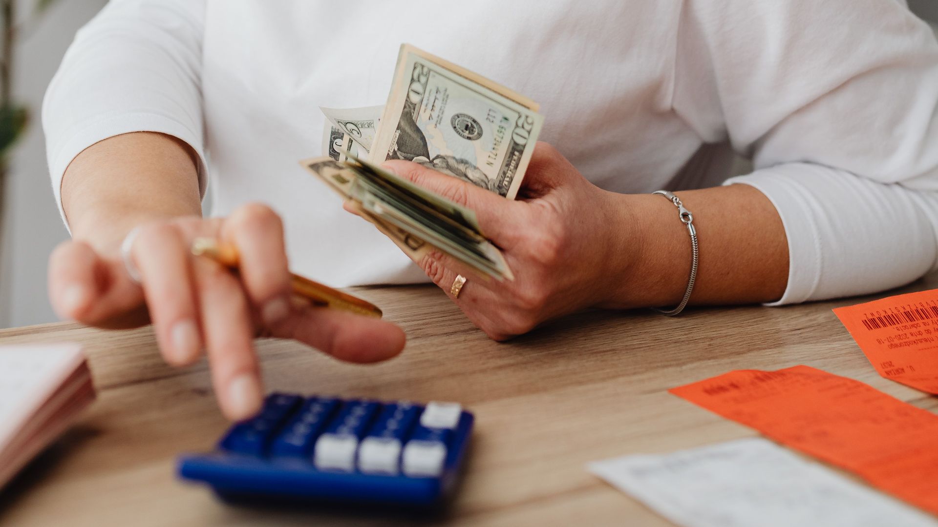 Woman using calculator and handling cash for financial planning at home.