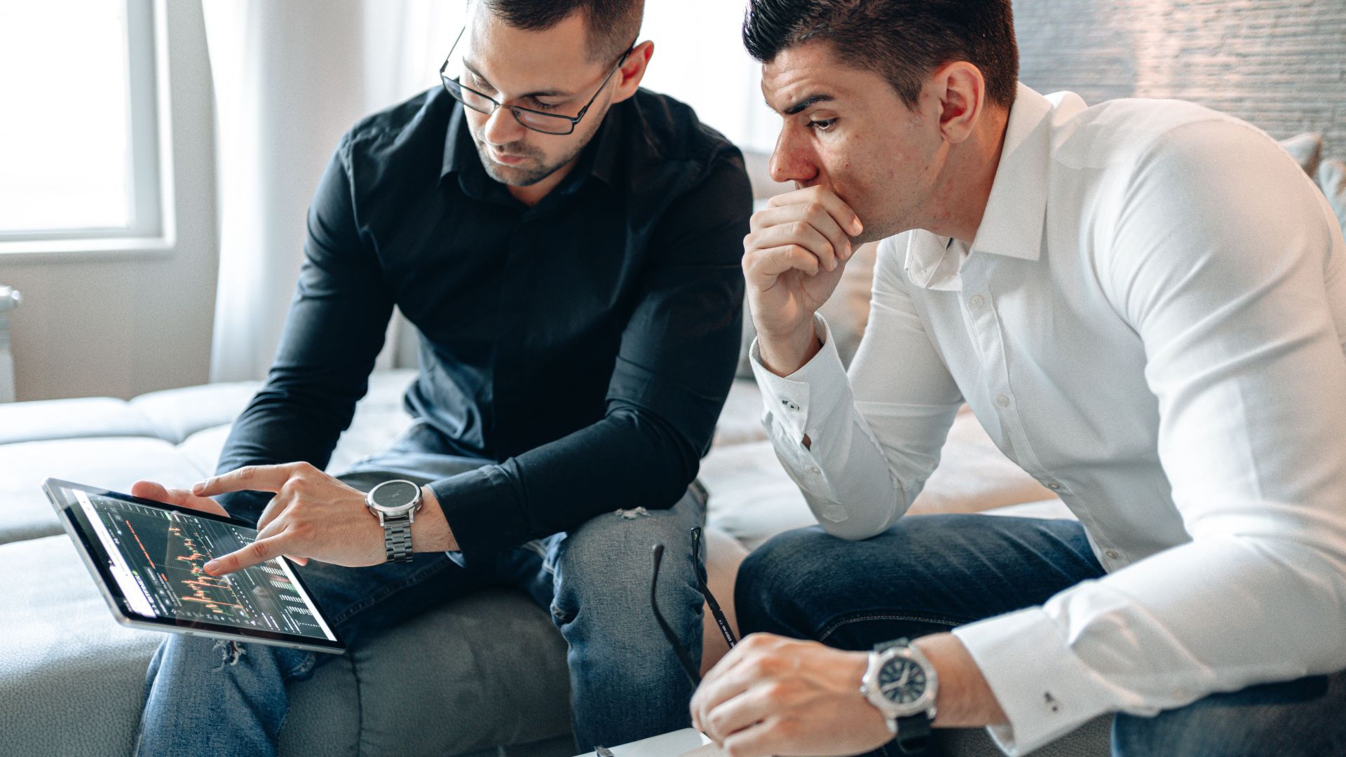 Two businessmen analyzing financial data on a tablet indoors.