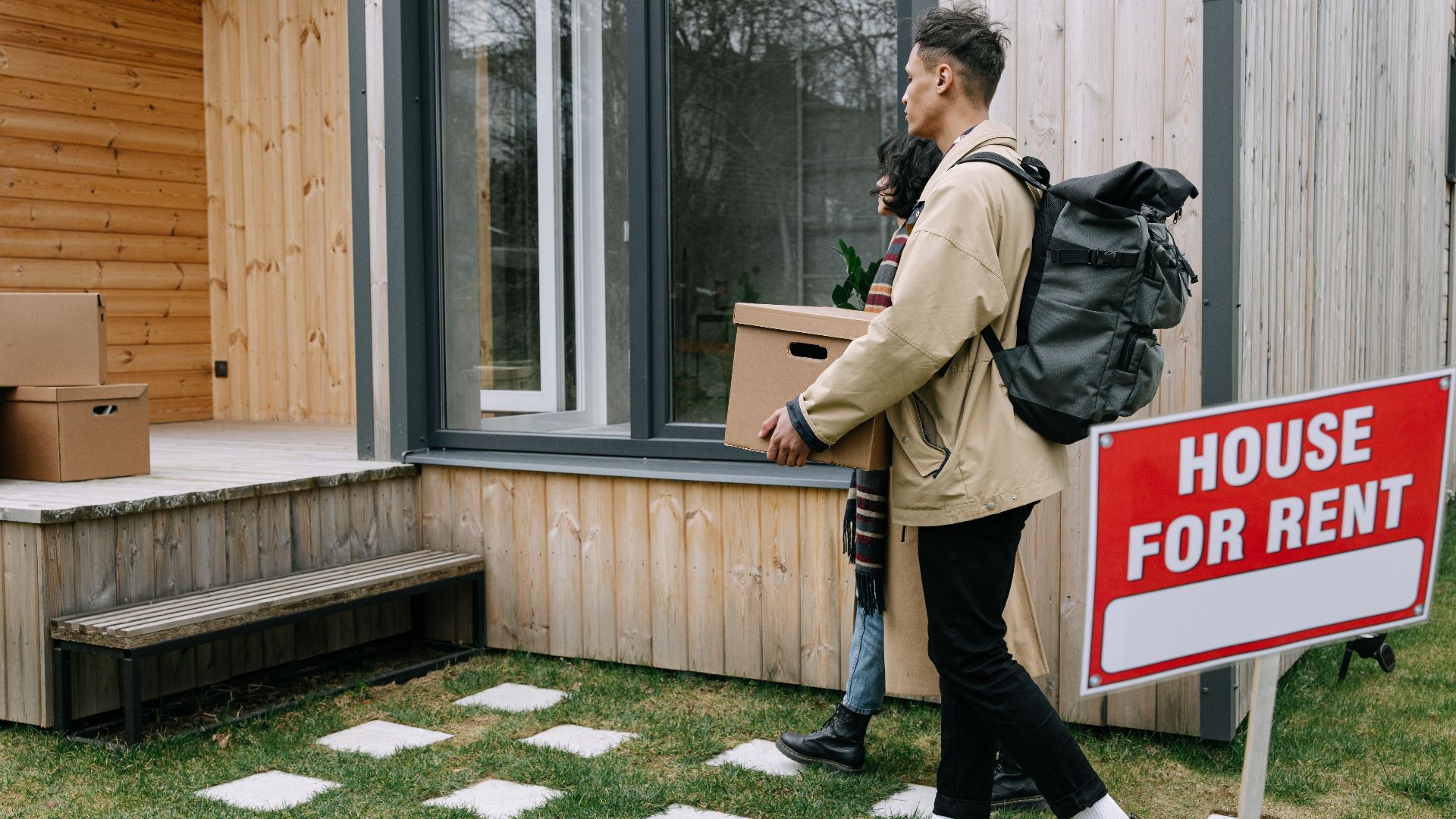 Young couple moving into a new rental home with boxes. Outdoor scene with a rental sign.