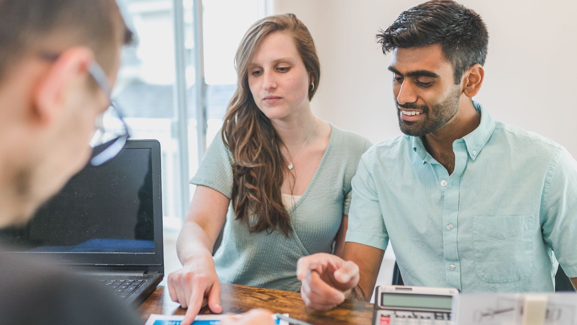 Young couple consulting with a financial advisor using a calculator and documents in a bright office setting.