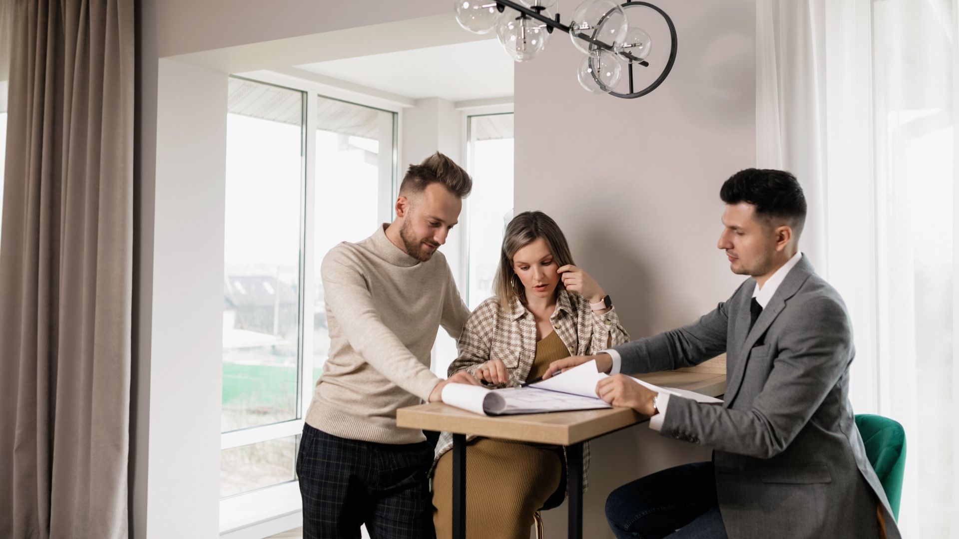 A couple consults with a real estate agent in a modern indoor setting, reviewing property documents.