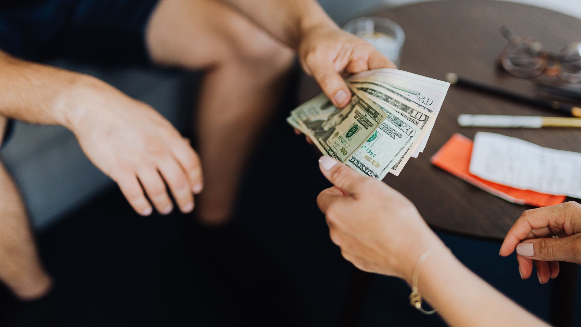 Close-up of hands exchanging US dollar bills, symbolizing a financial transaction or payment.
