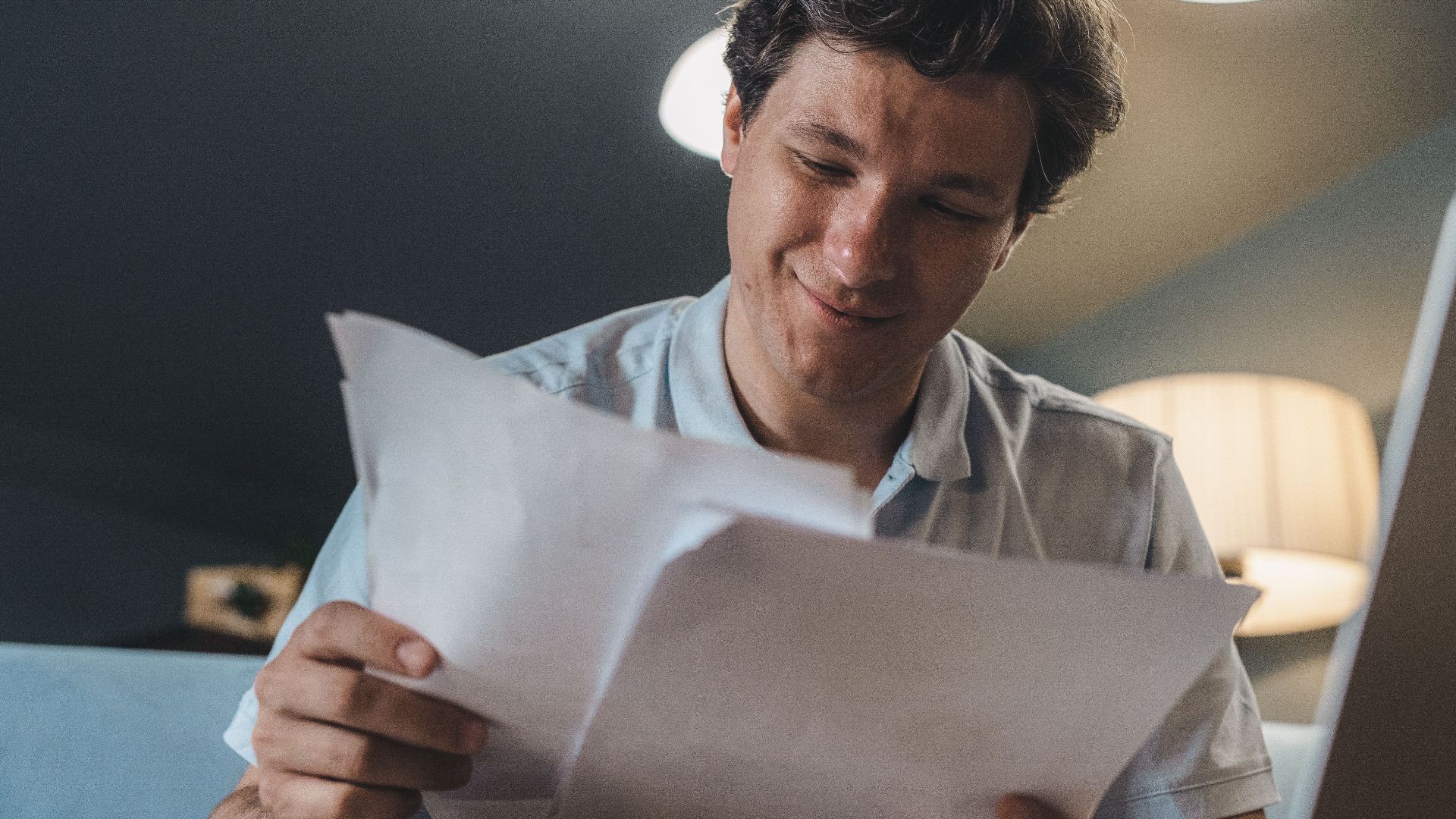 A cheerful man reading papers in a cozy indoor setting, radiating positivity.