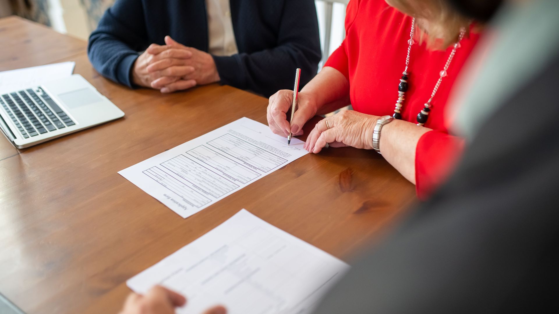 Two adults sign documents on a wooden table at a business meeting, emphasizing teamwork.