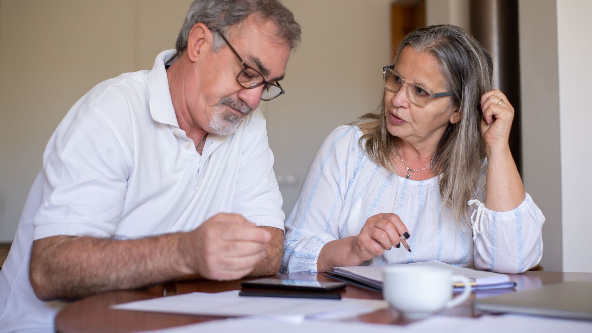 Senior couple reviewing documents and managing finances together at home, showing collaboration and care.