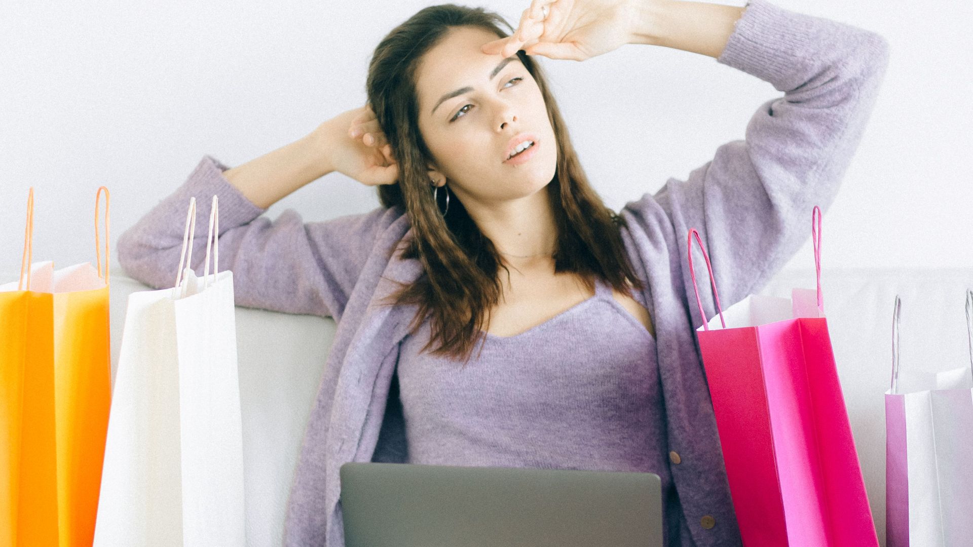 Young woman sitting on couch shopping online with colorful bags and laptop.