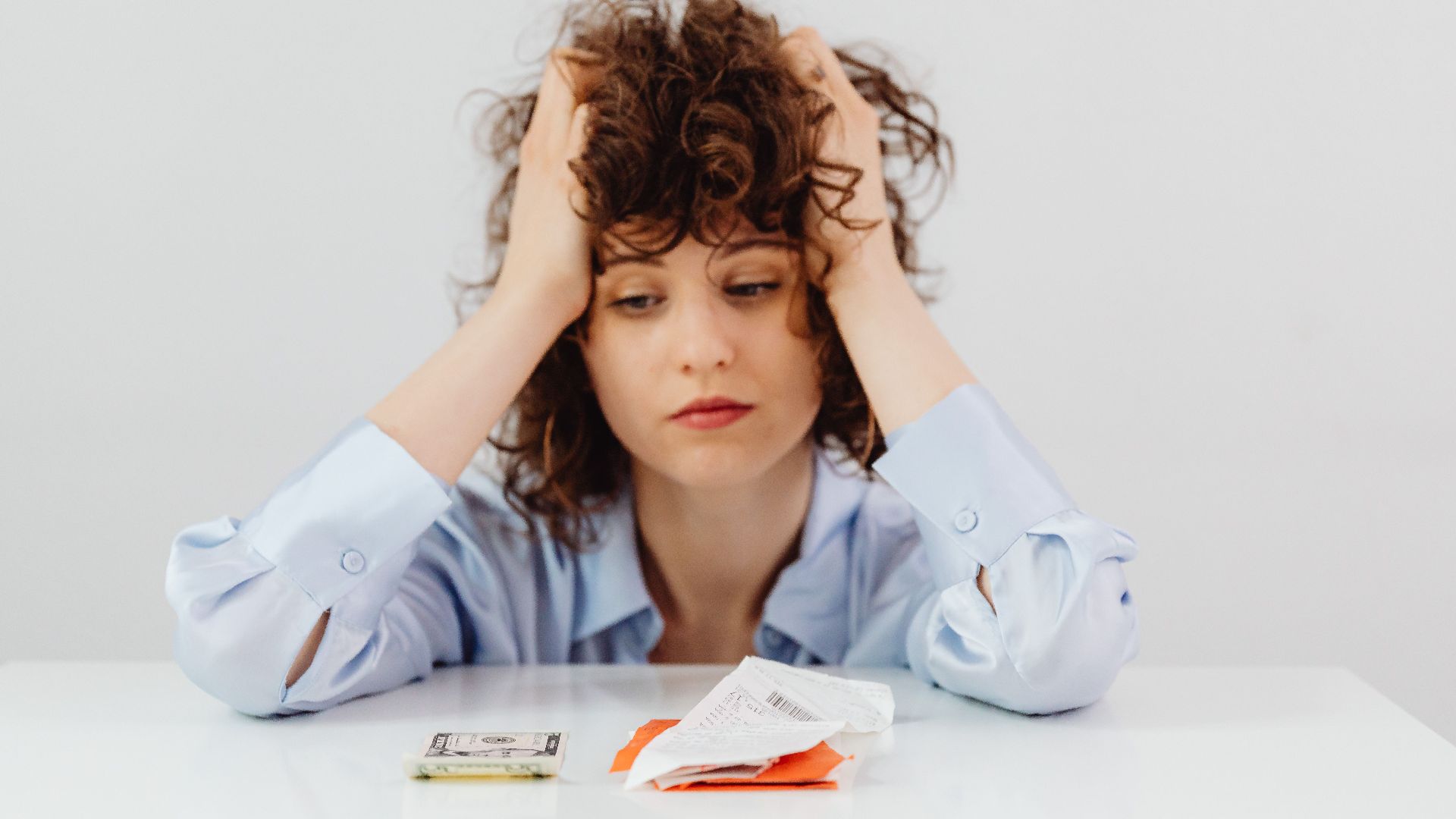 Woman in blue sleeves appears stressed while looking at receipts and money, symbolizing financial stress.