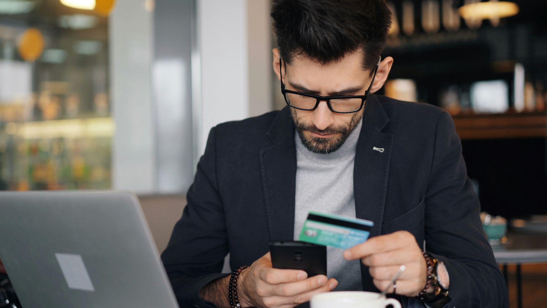 a man sitting at a table looking at his cell phone and holding a credit card