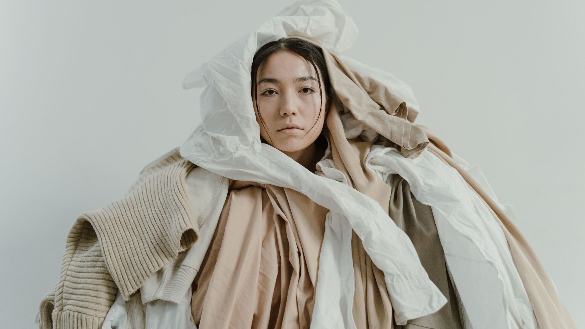 Artistic portrait of a woman in a pile of neutral toned clothes.