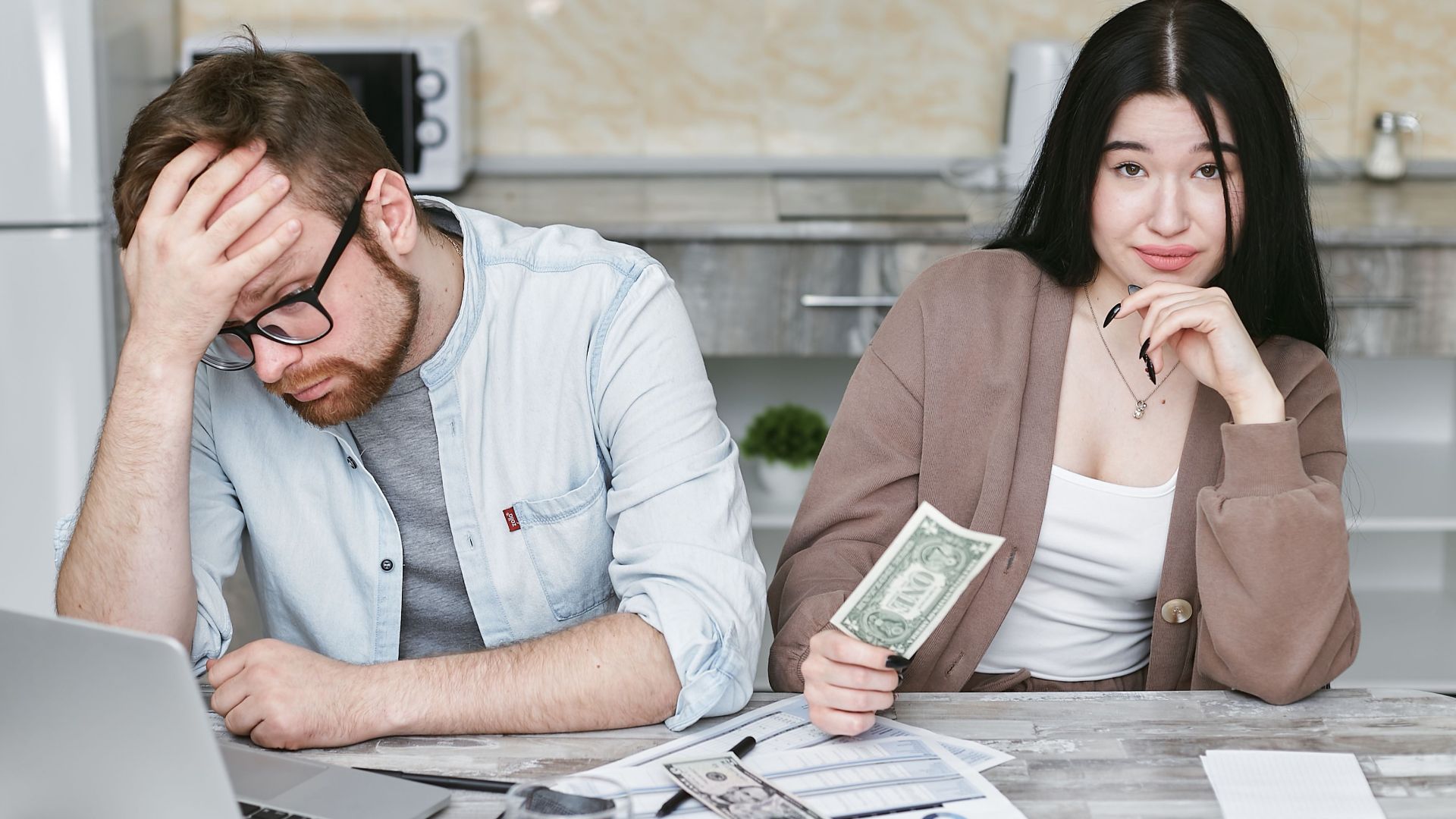 A couple managing their finances in a kitchen setting, showcasing money, debt, and budgeting challenges.