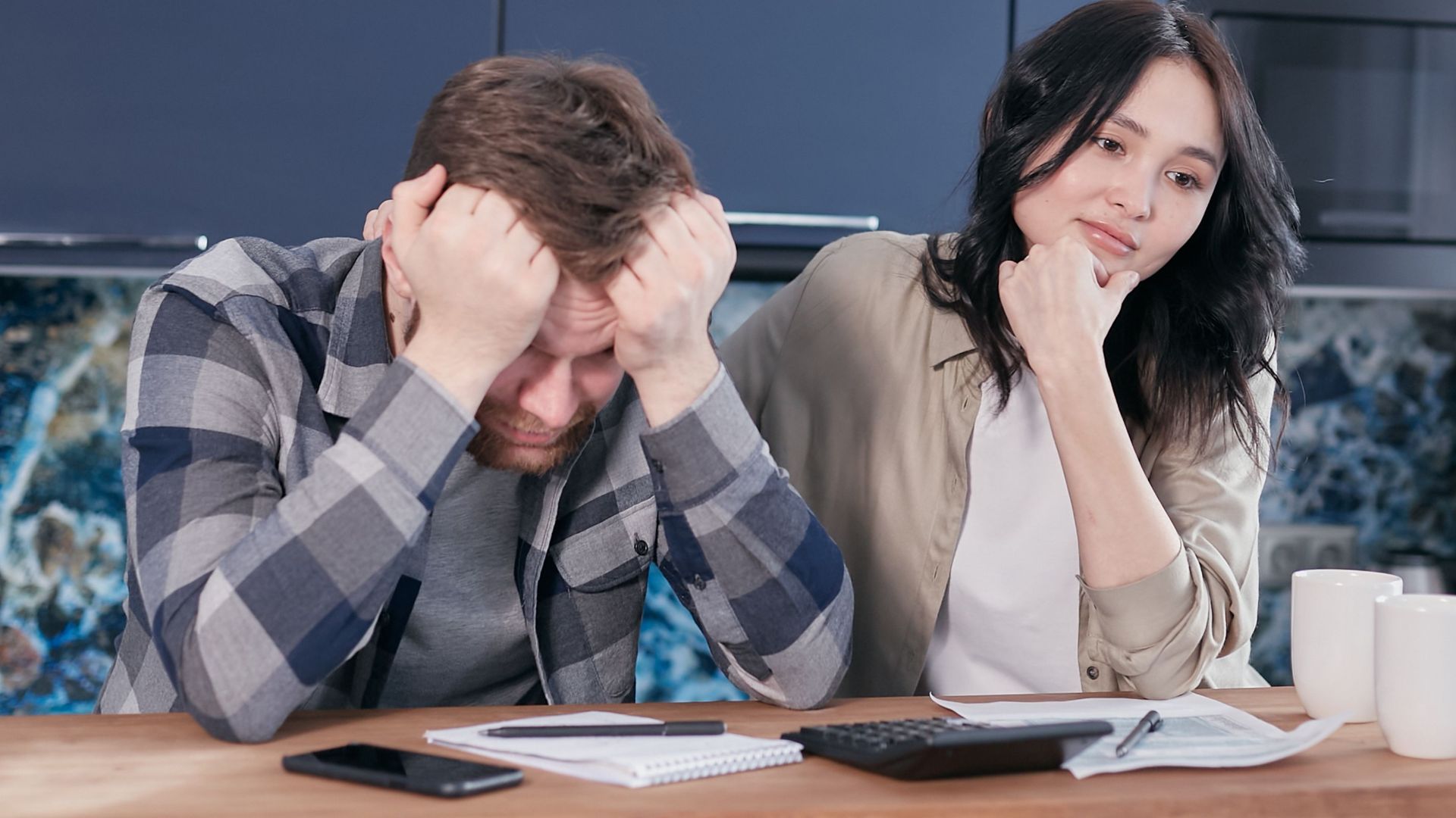 A couple looking worried while reviewing financial documents at a kitchen table.