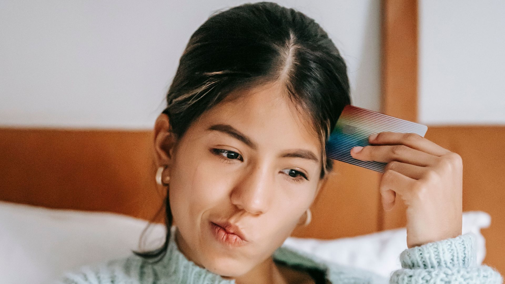 Young thoughtful ethnic female buyer with credit card and netbook sitting on bed at home